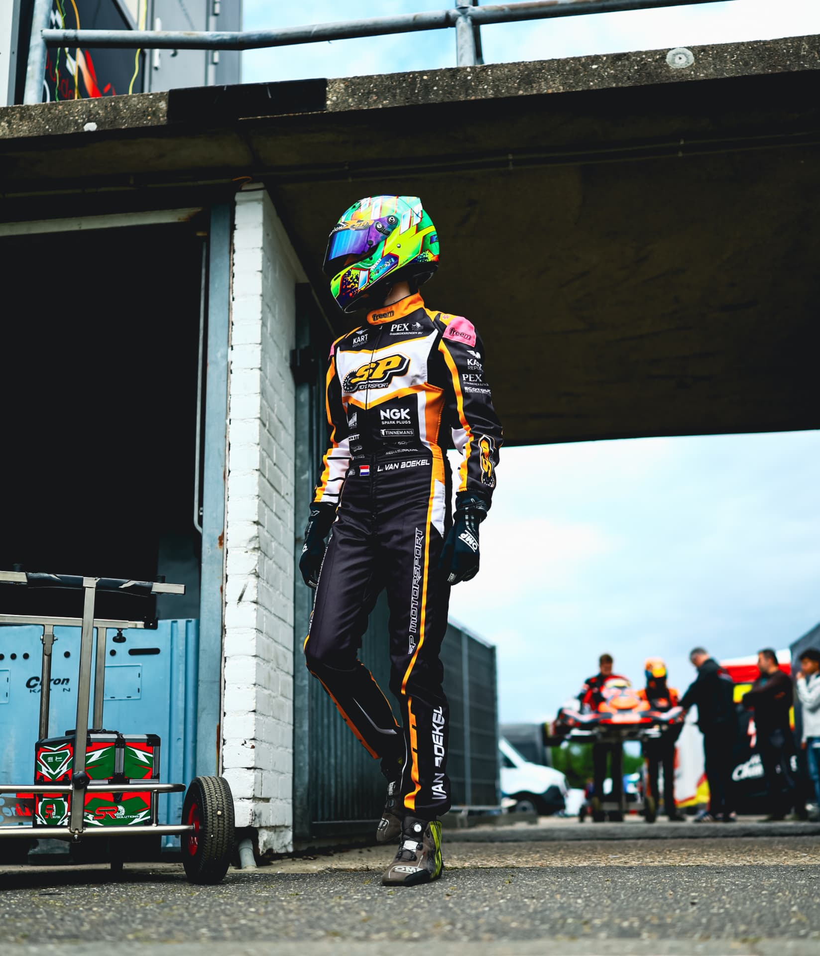 Lieke van Boekel in her race suit and helmet, leaning against a pit wall